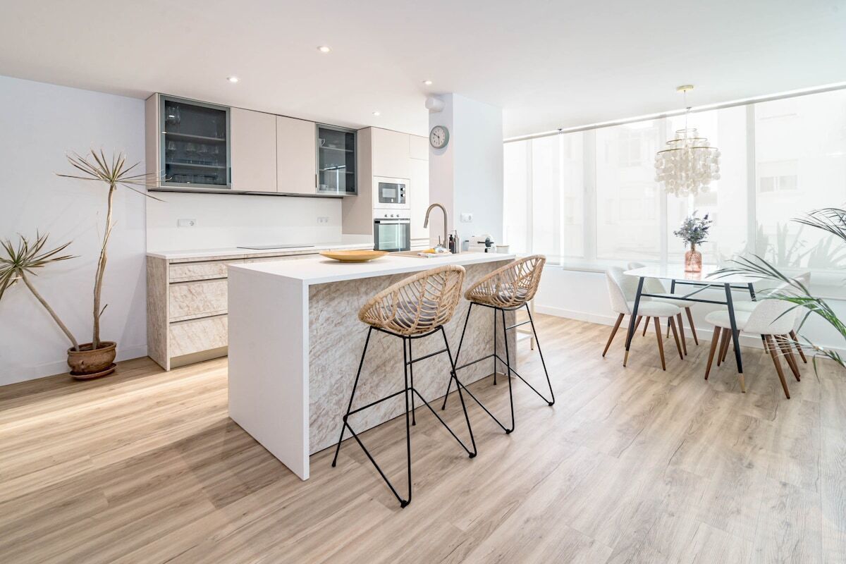 A modern kitchen with a central island, bar stools, and a dining area with a chandelier.