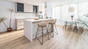 A modern kitchen with a central island, bar stools, and a dining area with a chandelier. - Eac3f- Modern & Light Apartment Steps From the sea (Estepona)