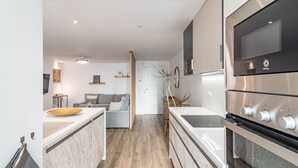 A modern kitchen with a central island, built-in oven, and a seating area with a sofa and coffee table. - Eac3f- Modern & Light Apartment Steps From the sea (Estepona)