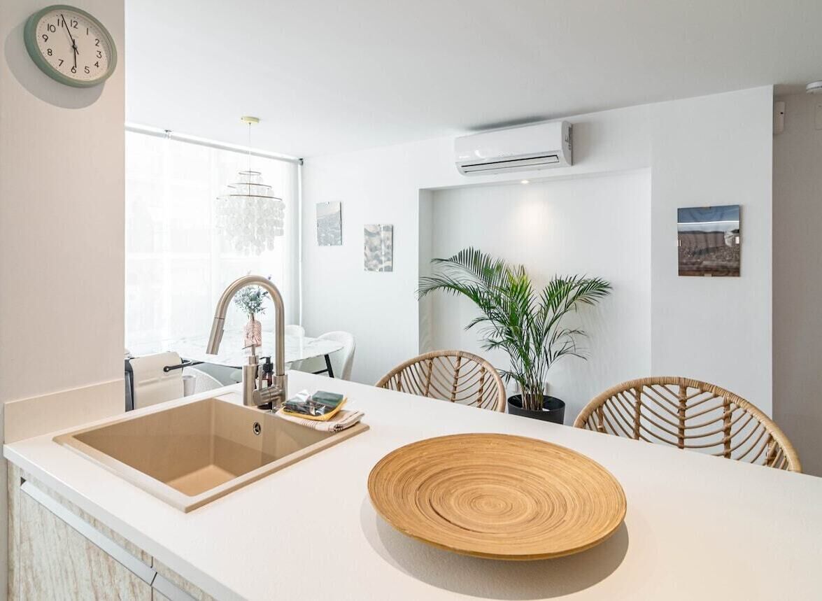 A modern kitchen with a sink, dining table, chairs, and a potted plant.
