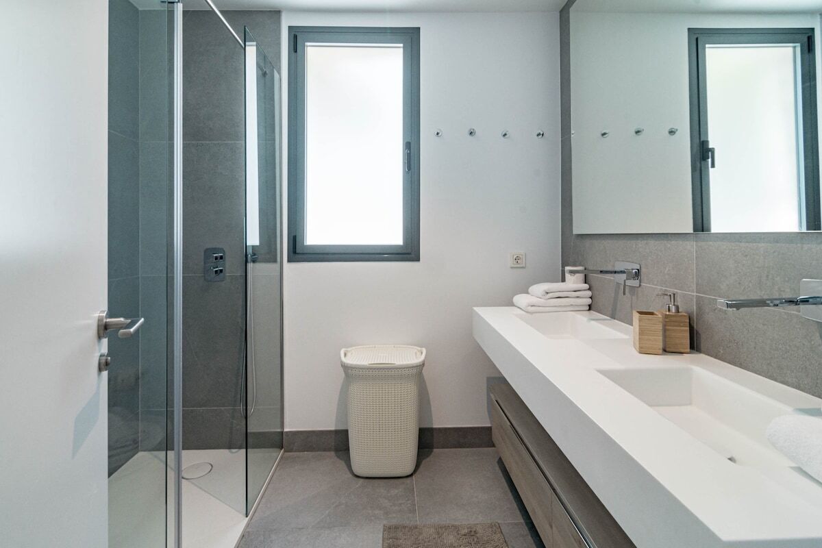 A modern bathroom with a glass shower enclosure, a large mirror, and a white vanity with a sink.