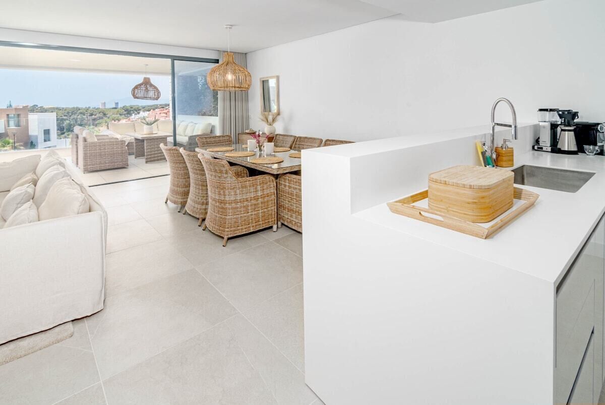 Une cuisine moderne dotée d’un grand îlot central, d’un coin repas avec des meubles en osier et offrant une vue sur la ville.