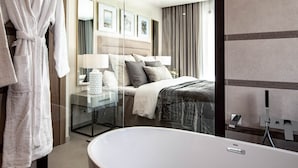 Una habitación de hotel moderna con un baño de vidrio y una cama grande con cabecera, además de una bata colgada en un gancho.
