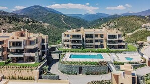 Un moderno complejo residencial con varias edificaciones, una piscina central y un paisaje montañoso de fondo.