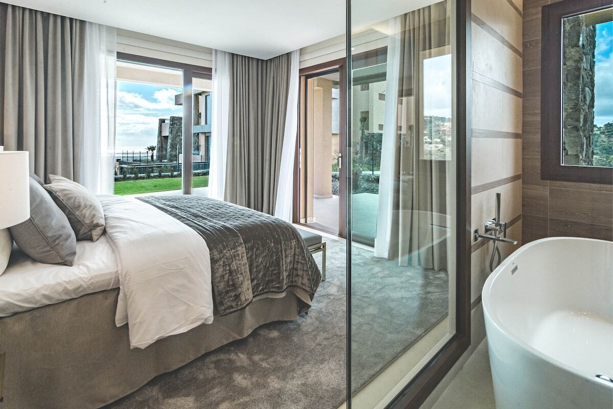 Un dormitorio moderno con una cama grande, cabina de ducha de vidrio y vistas a un paisaje verde.