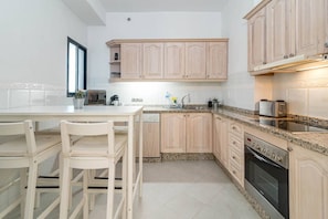 Una cocina moderna con armarios de madera clara, encimera de granito y electrodomésticos de acero inoxidable.