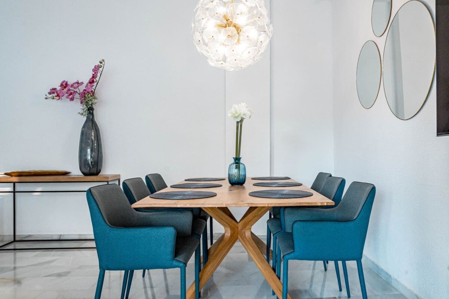 Un espace repas moderne avec une table en bois, des chaises bleues et un luminaire suspendu.