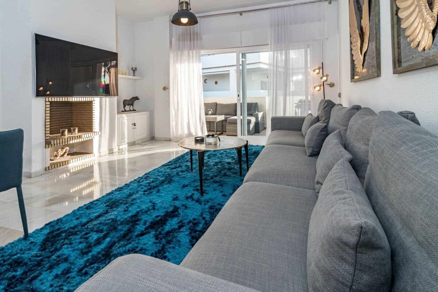 Una sala de estar moderna con un sofá gris, un felpudo azul y un televisor de pantalla plana montado en la pared.