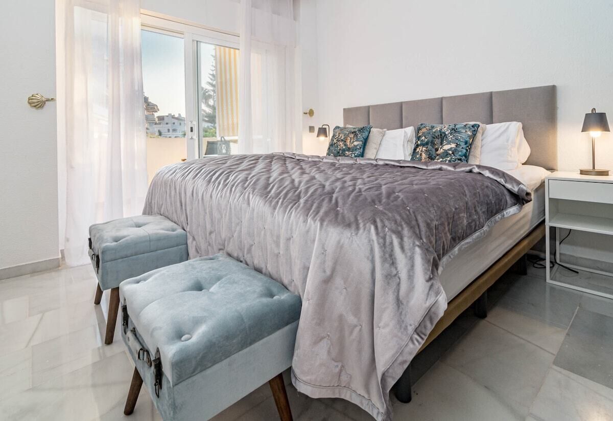 A modern bedroom with a large bed, a bench, and a nightstand.