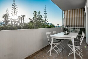 Un balcón con mesa y sillas, un toldo a rayas y vistas a árboles y edificios.