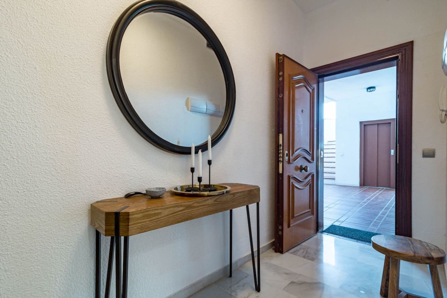 A hallway with a wooden console table, a round mirror, and a door leading to another room.