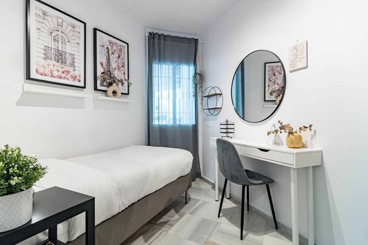 A bedroom with a bed, a desk, a chair, a mirror, and framed pictures on the wall.