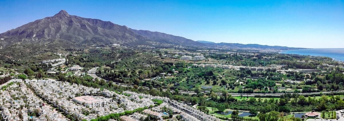 Un paisaje montañoso con un pueblo en primer plano y una masa de agua a lo lejos.