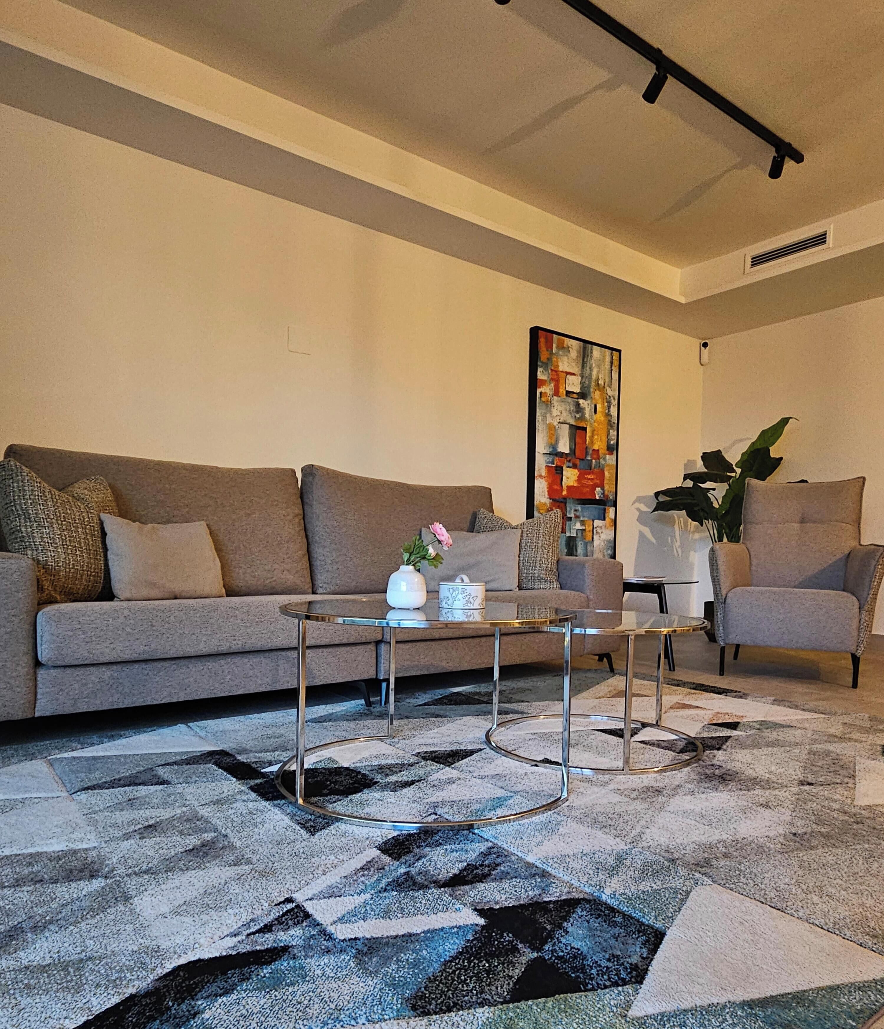 A living room with a sofa, a coffee table, a chair, a painting, and a plant.