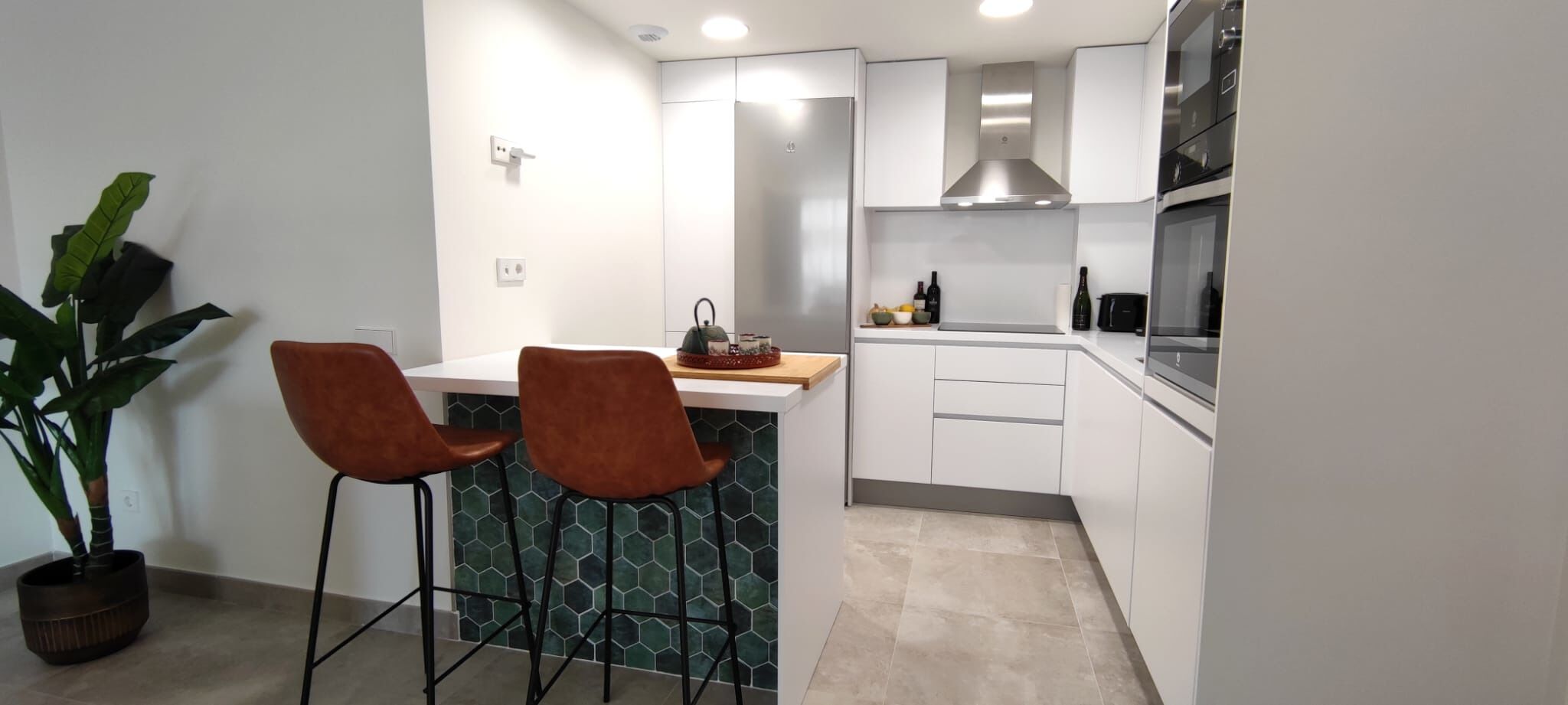 Una cucina moderna con mobili bianchi, un frigorifero in acciaio inossidabile, un lavello e due sgabelli da bar.