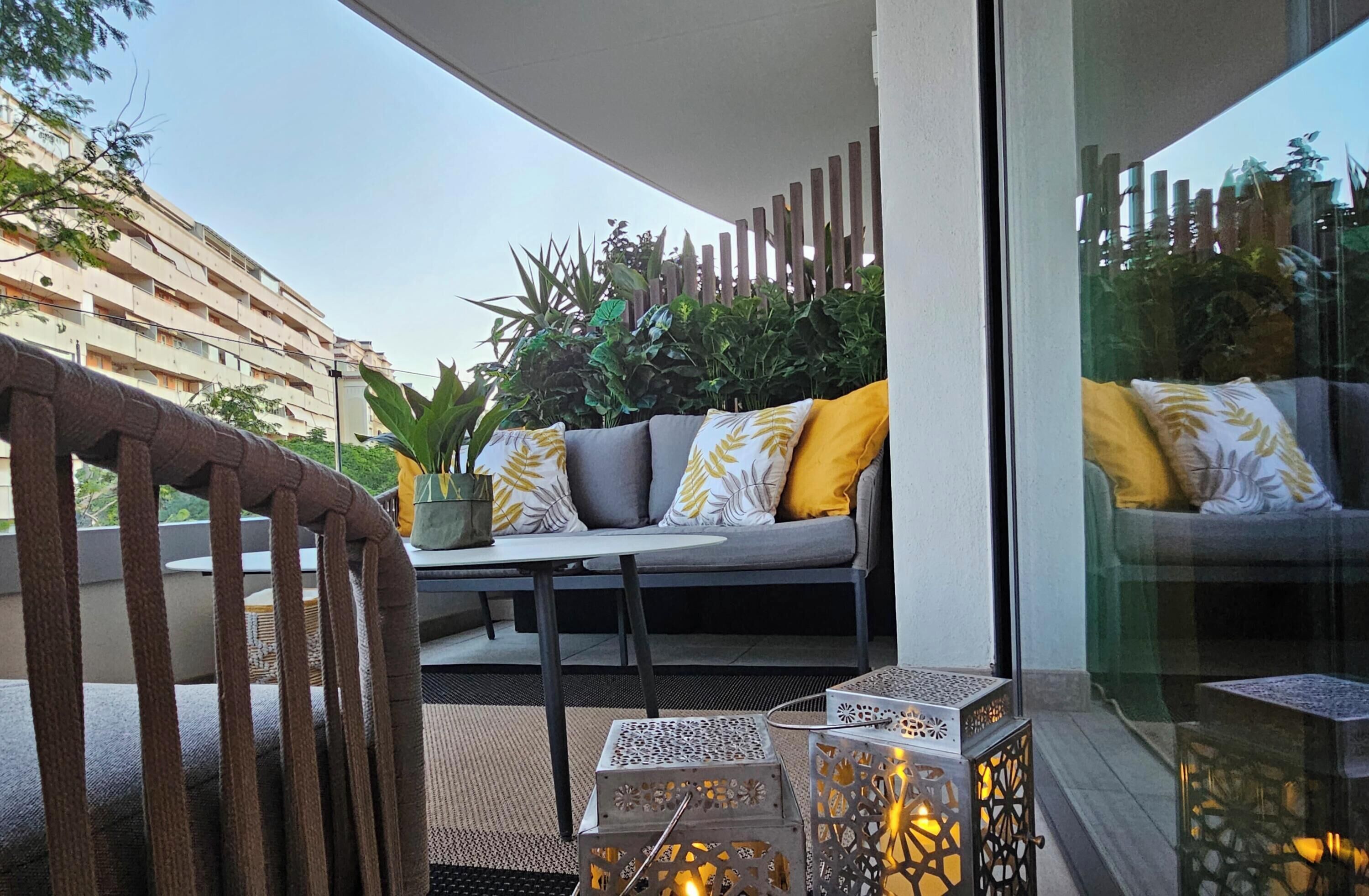 A balcony with a sofa, cushions, potted plants, and decorative lanterns.