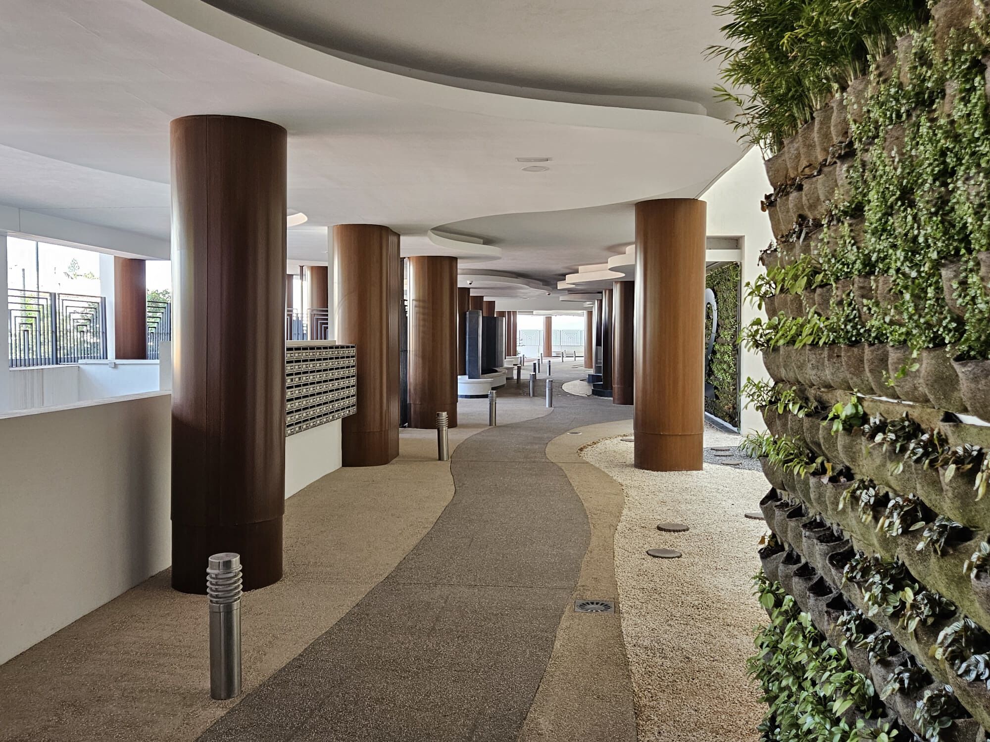 Un pasillo con pilares de madera, suelo con diseño de guijarros y una pared de jardín vertical.