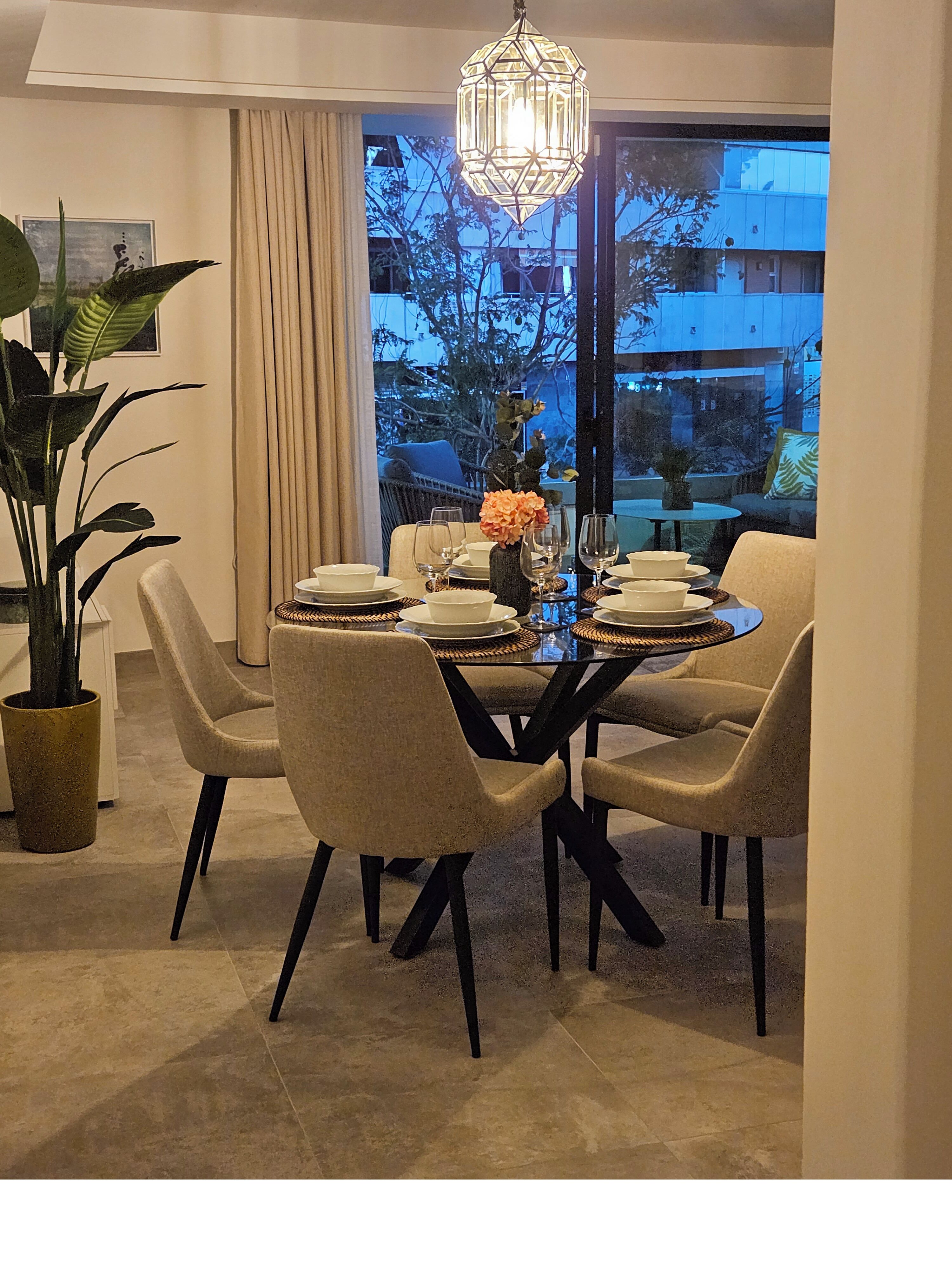 Un espace repas comprenant une table ronde, des chaises, un lustre et une vue dégagée grâce à de grandes fenêtres.