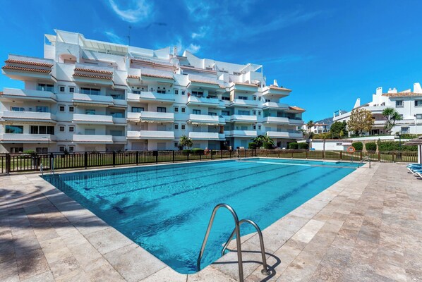 A swimming pool with a metal ladder, surrounded by a tiled deck, and a multi-story building with balconies in the background. - Rg325 - Great 2 Bed Apt, Close to Puerto Banus (Marbella)