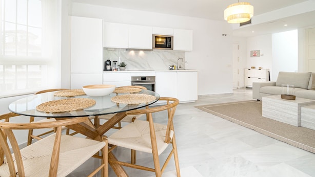 A modern kitchen with white cabinets, a built-in microwave, and a dining area with a glass table and woven chairs. - Lnm530 - Great Location With Private Roof Terrace (Marbella)