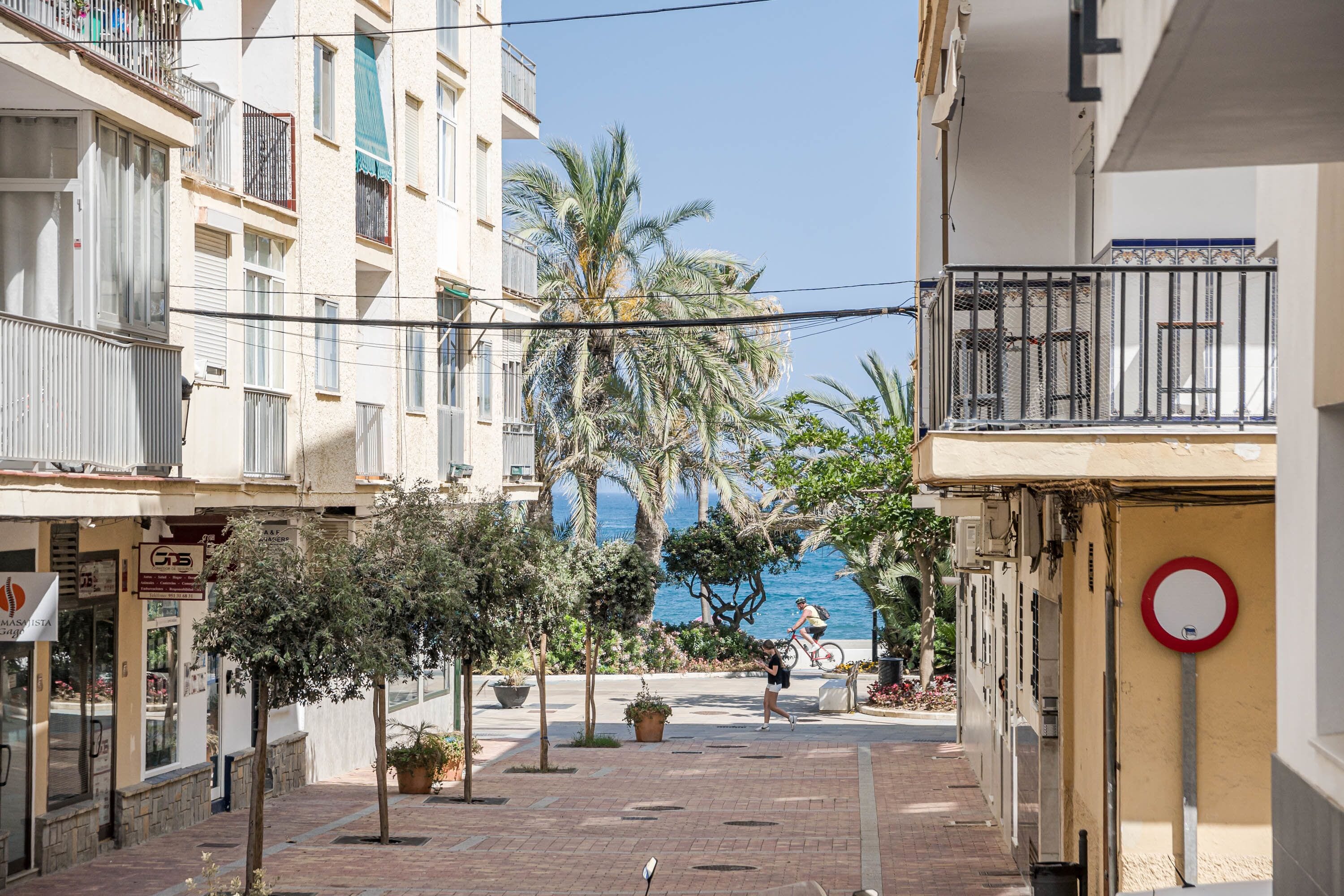 Une rue étroite en milieu urbain, avec des immeubles, un piéton et un cycliste.