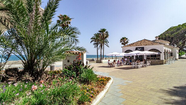 A coastal building with outdoor seating, palm trees, and a view of the sea. - Le2c Luxury New Build Apartment Near the Beach (Estepona)