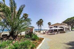 A coastal building with outdoor seating, palm trees, and a view of the sea. - Le2c Luxury New Build Apartment Near the Beach (Estepona)