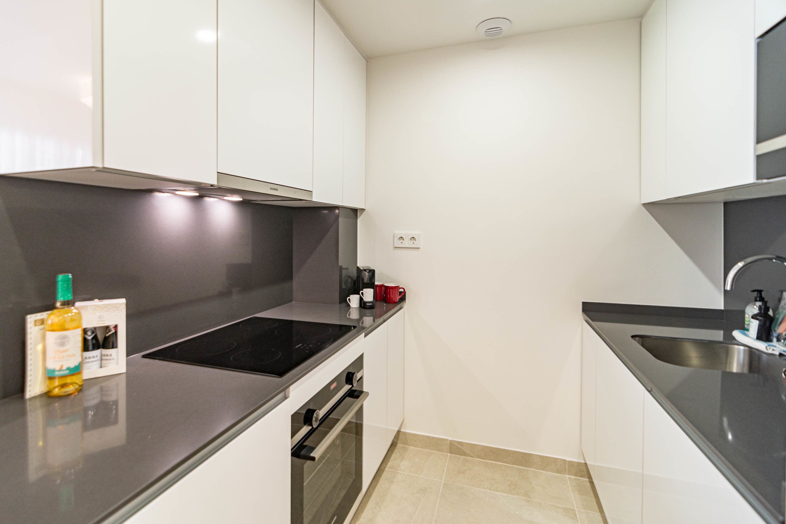 A modern kitchen with white cabinets, a black countertop, a built-in oven, and a stainless steel sink.