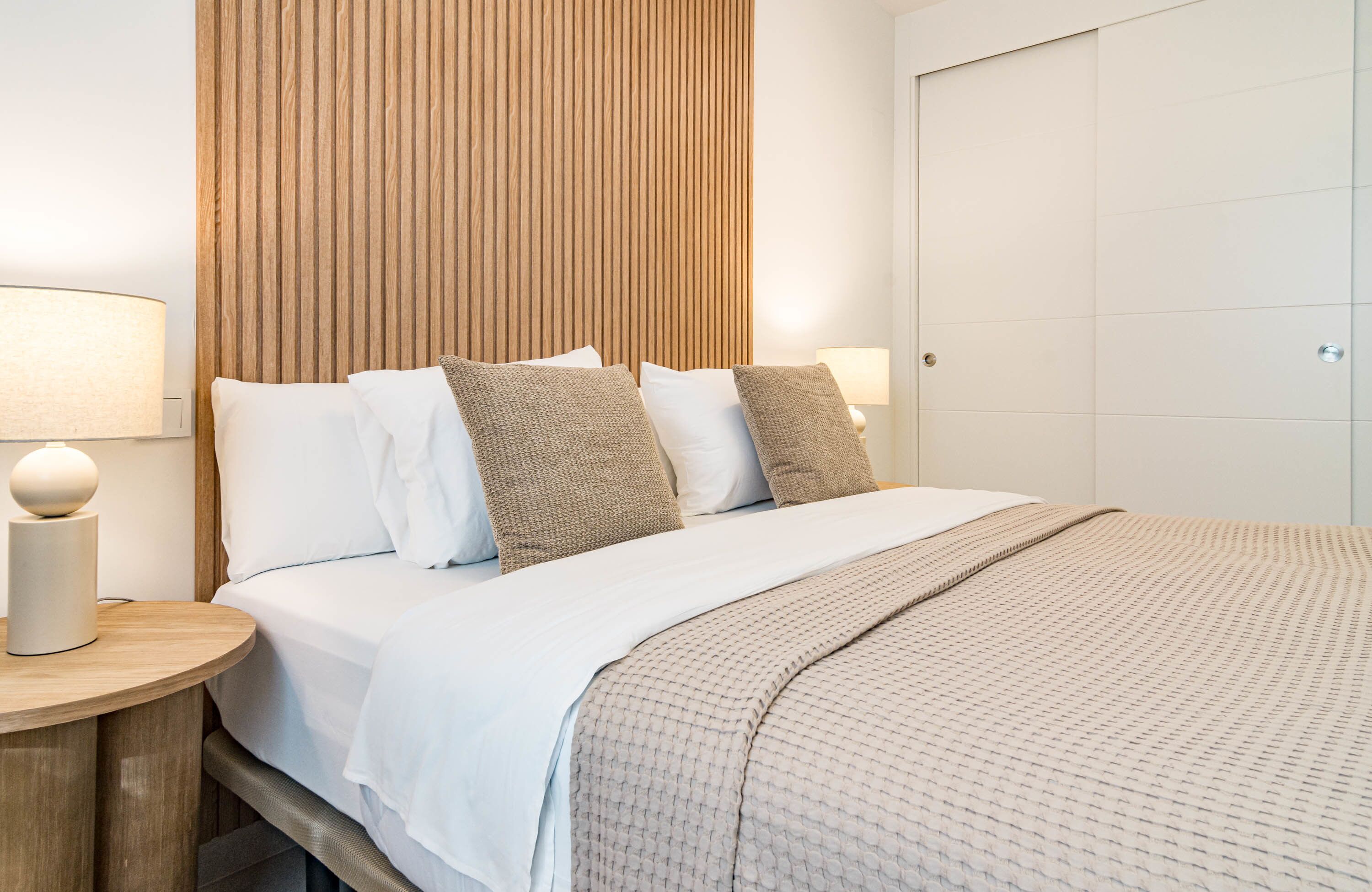 A hotel room with a bed, a wooden headboard, a bedside table with a lamp, and a wardrobe.