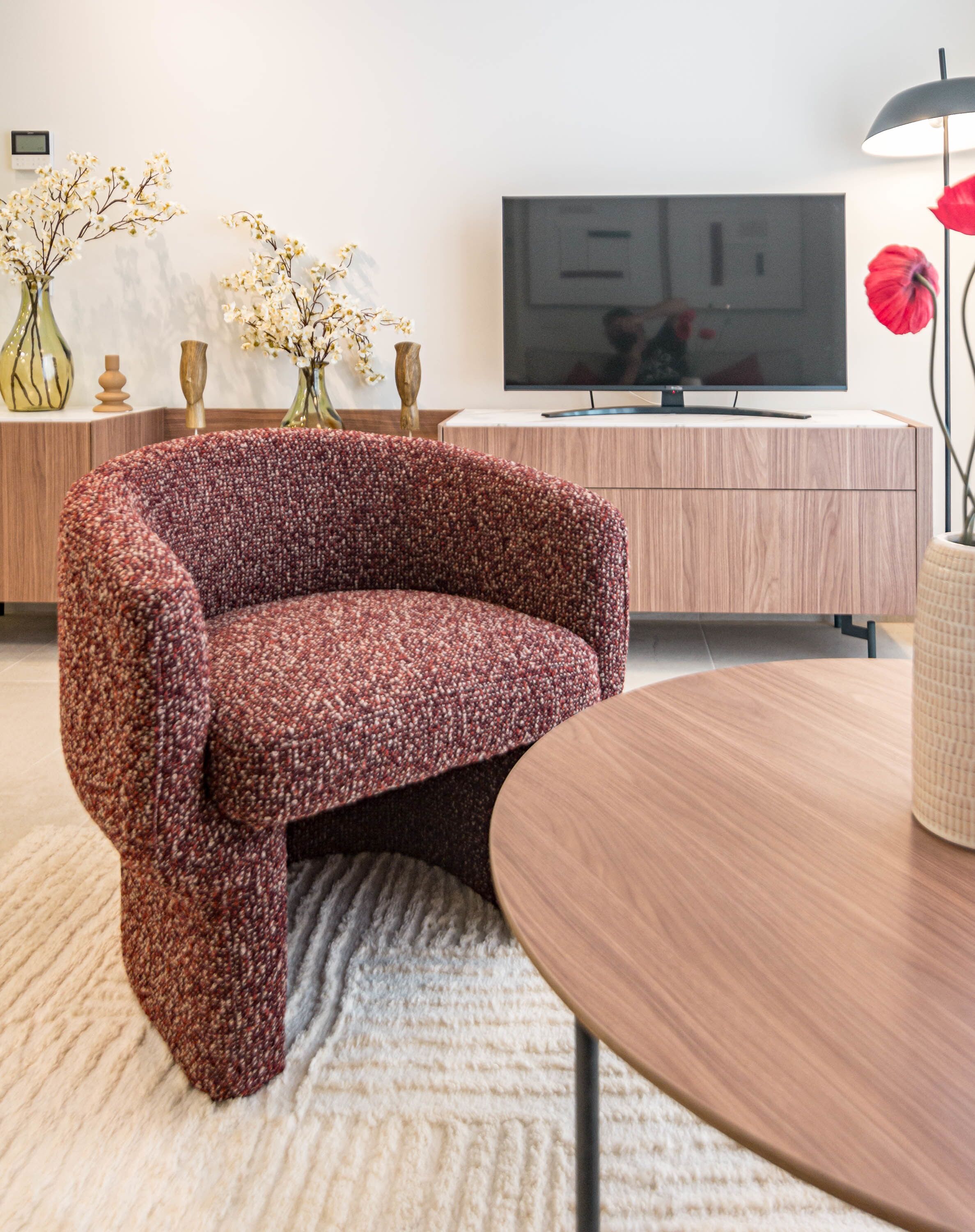 A modern living room with a patterned sofa, a round wooden table, a flat-screen TV, and decorative vases.
