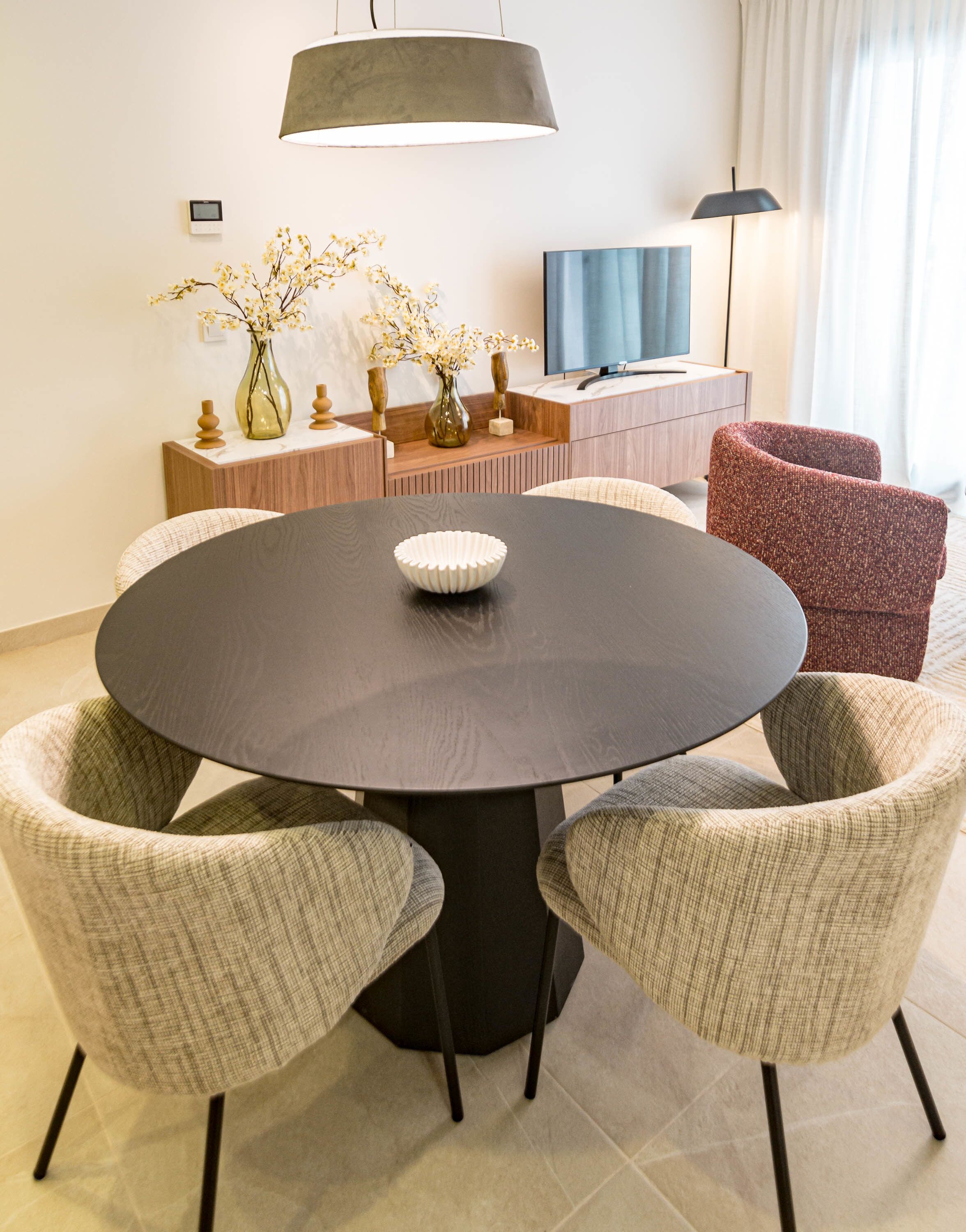 Un coin repas comprenant une table ronde, quatre chaises, un vase avec des fleurs, un téléviseur et une lampe.