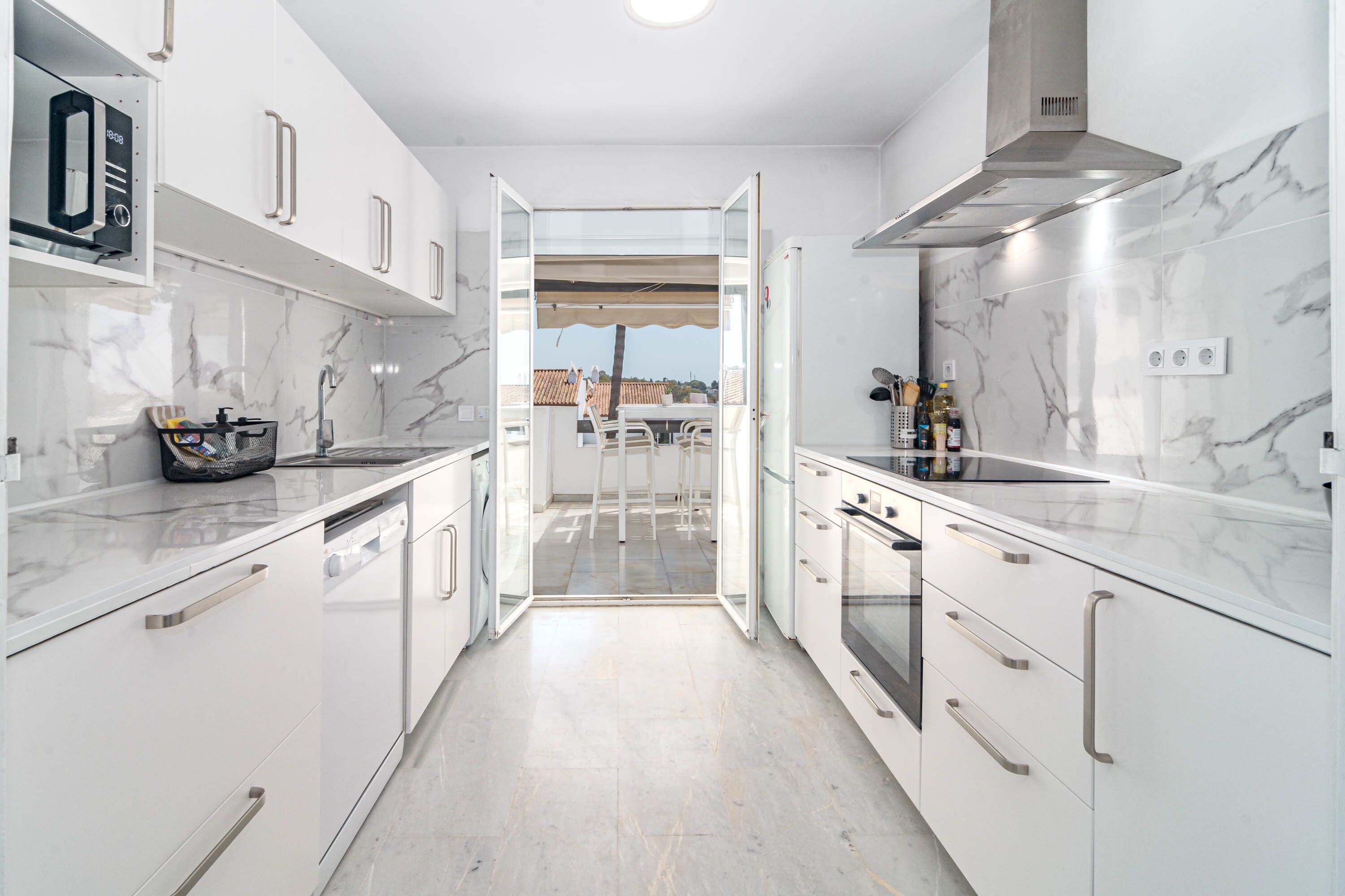 Una cocina moderna con armarios blancos, horno empotrado y vistas al exterior.