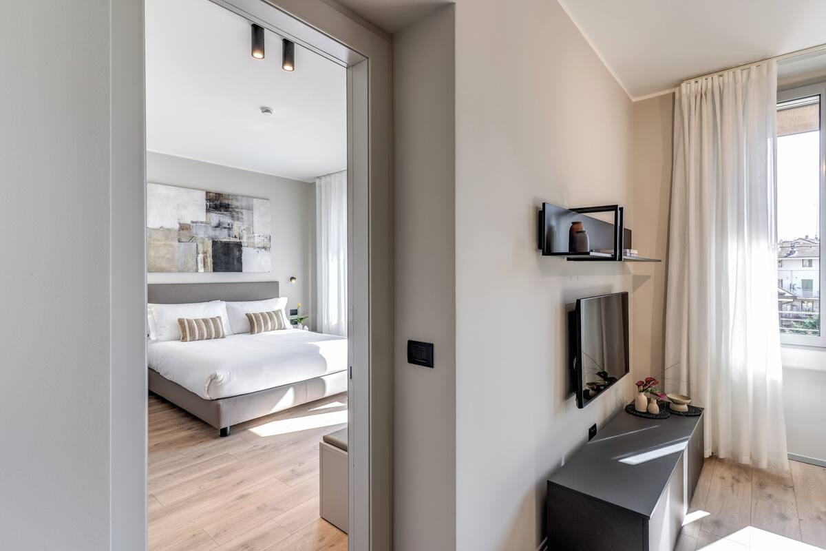 A modern hotel room with a bed, a flat-screen TV, a small console table, and a large window with curtains.