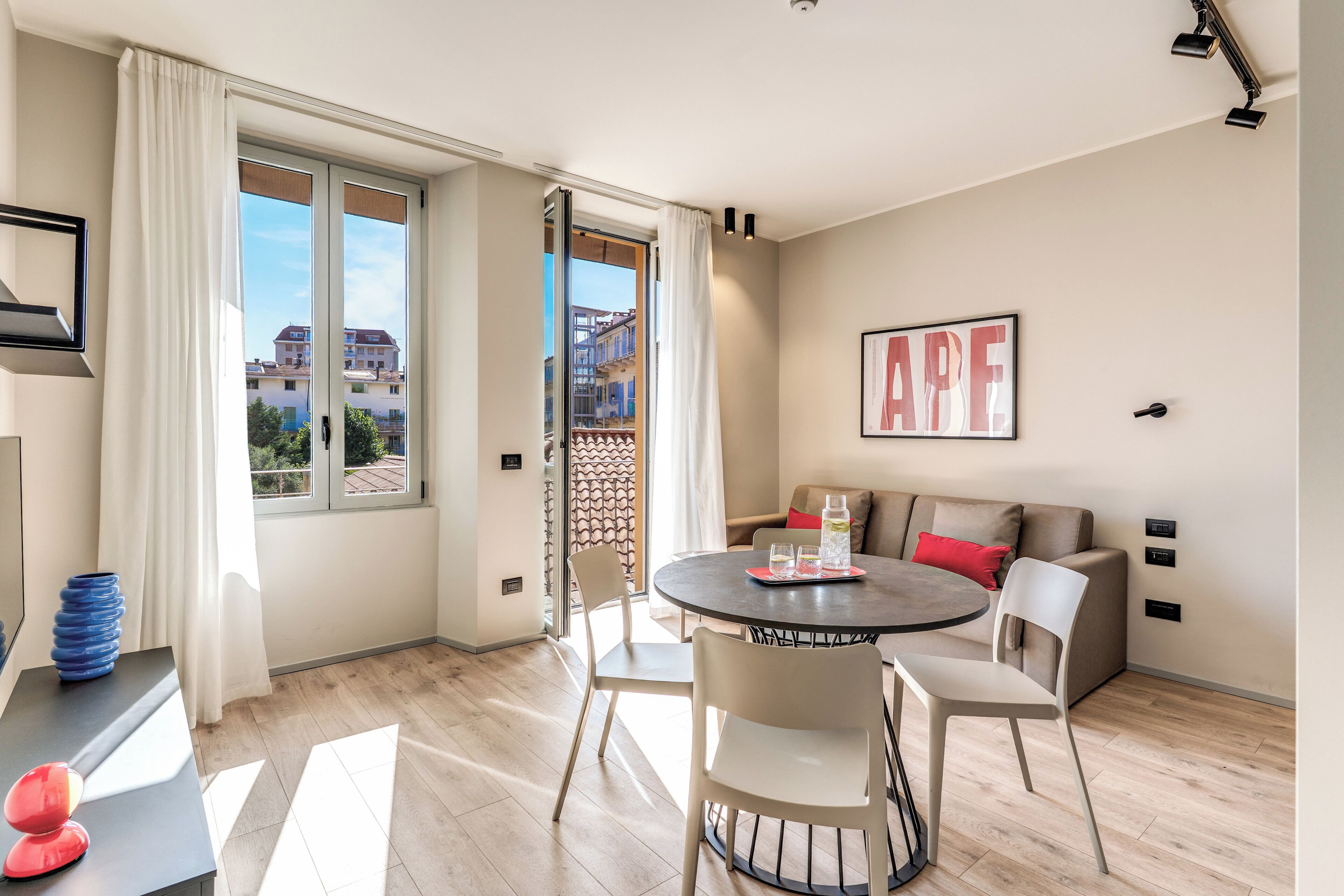 Een moderne woonkamer met een ronde tafel, stoelen, een bank en een groot raam met gordijnen.