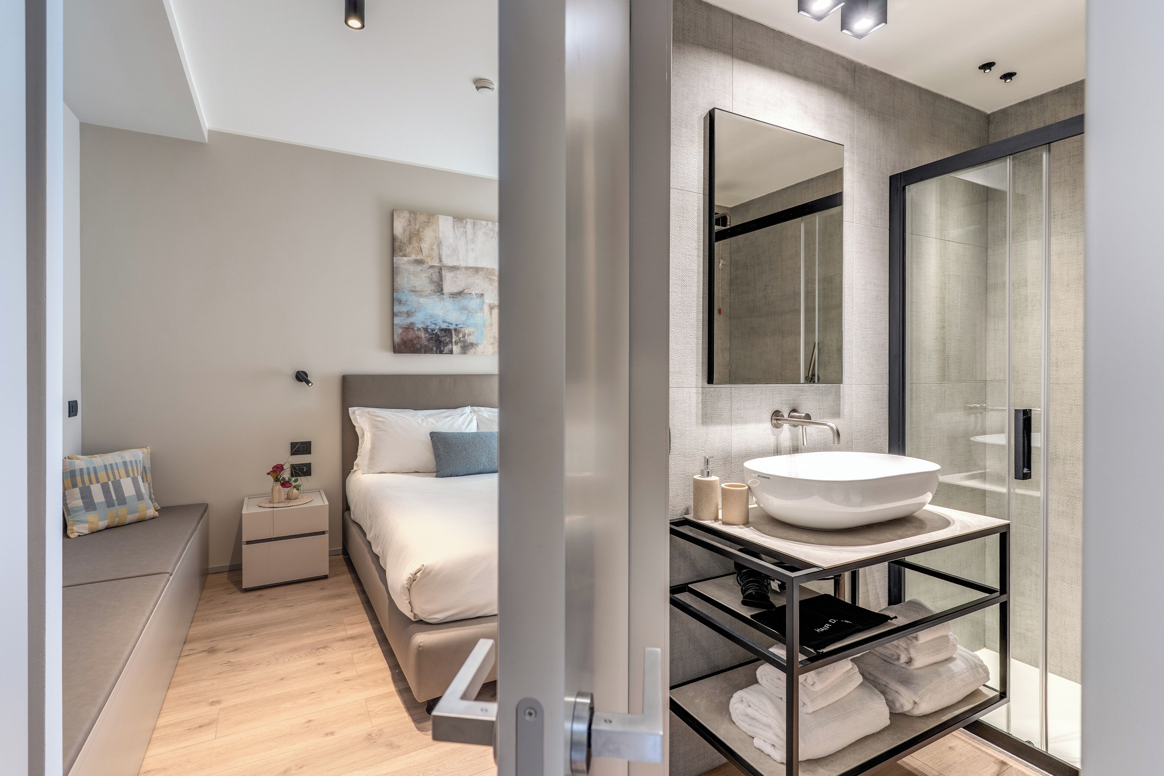 A modern bedroom with a bed, bedside table, and a glass shower enclosure.