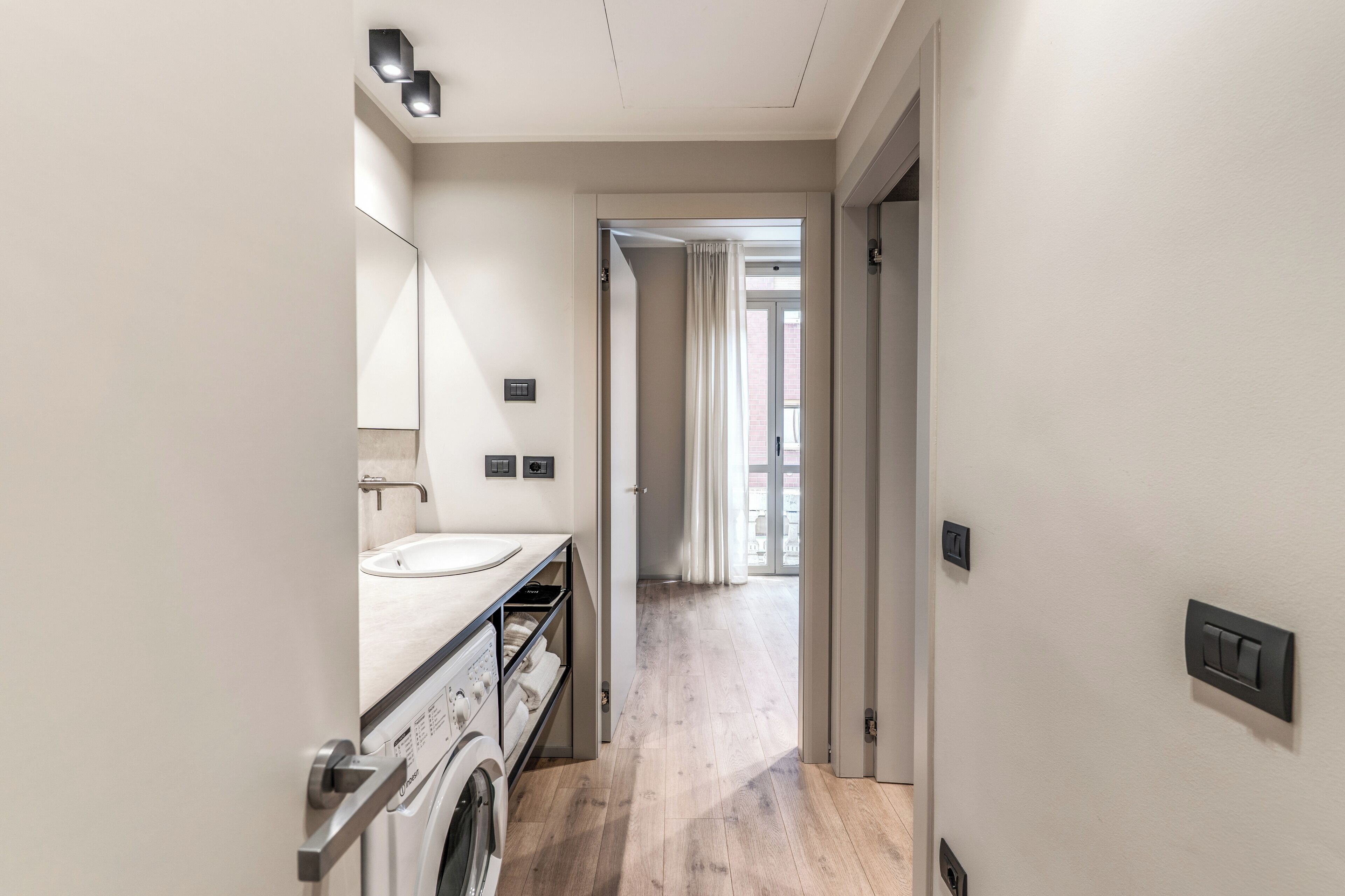 Een moderne badkamer met een wasmachine, een wastafel en een spiegel.
