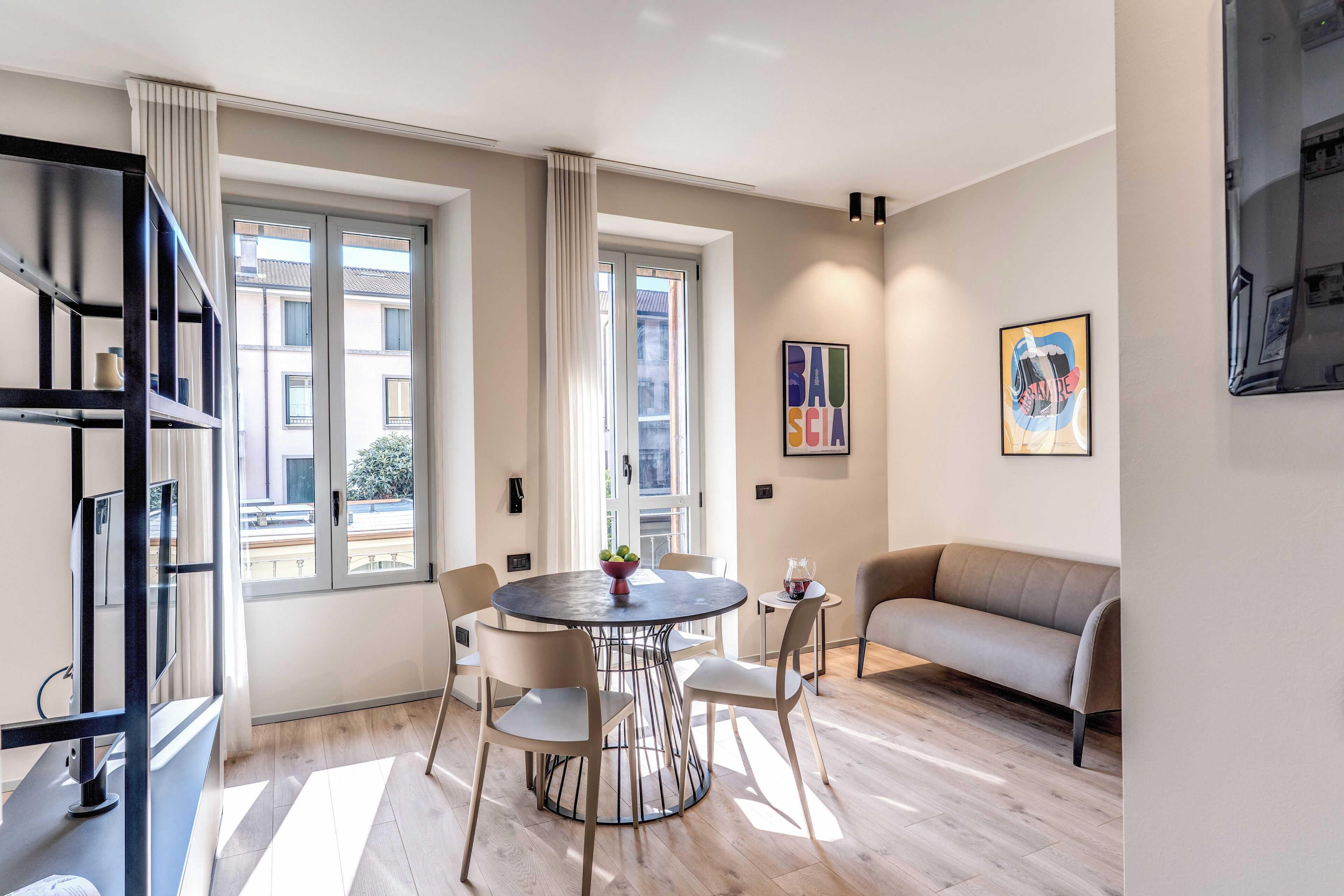 A modern living room with a round dining table, two chairs, a sofa, and a bookshelf.