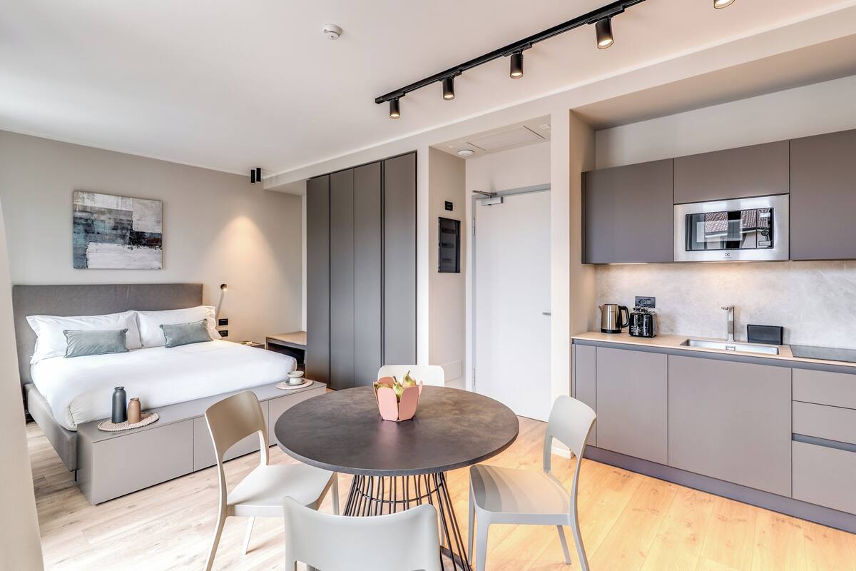 A modern hotel room with a bed, bedside table, and a round dining table with chairs.