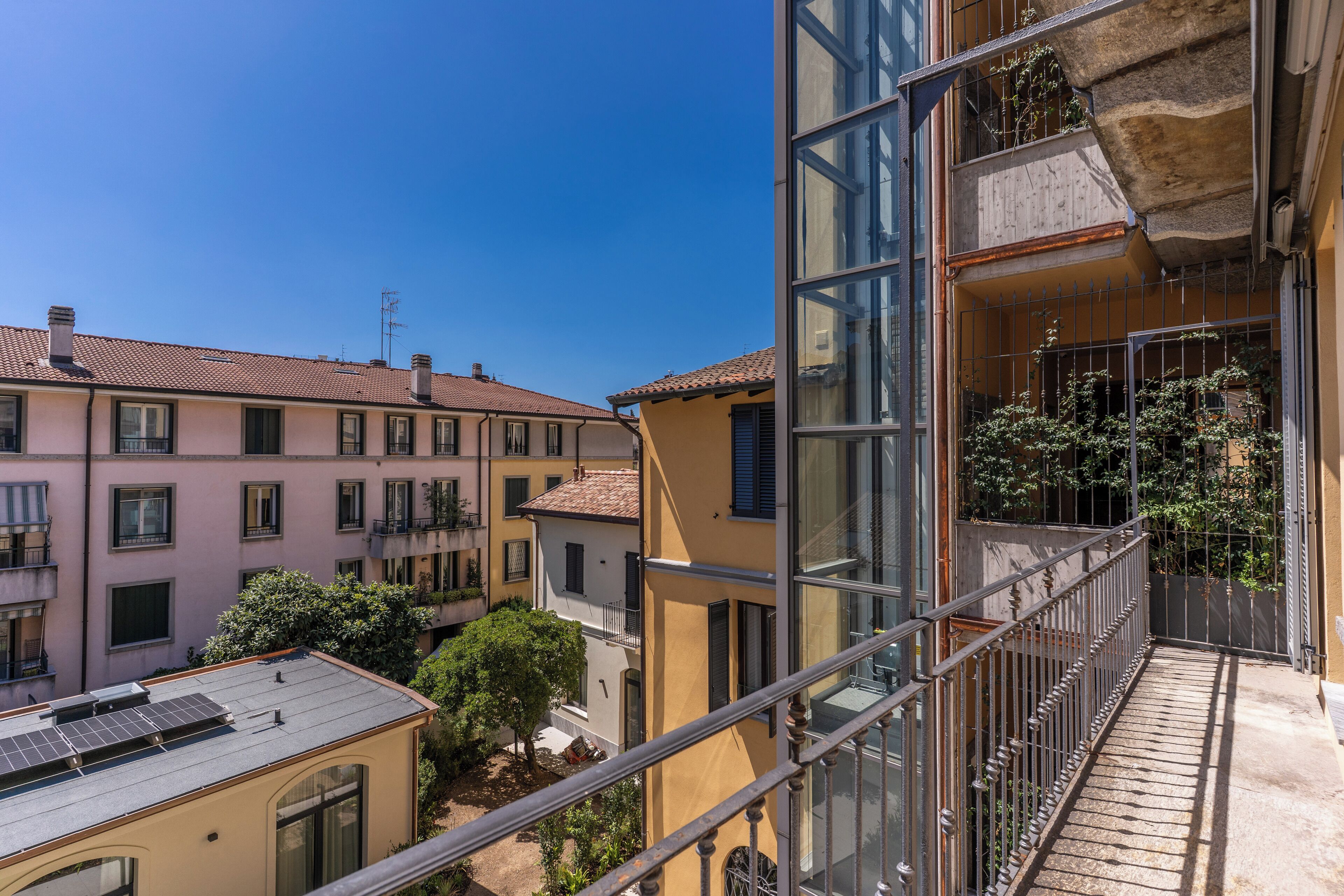 A multi-story residential building with balconies, a clear sky, and a courtyard with trees.