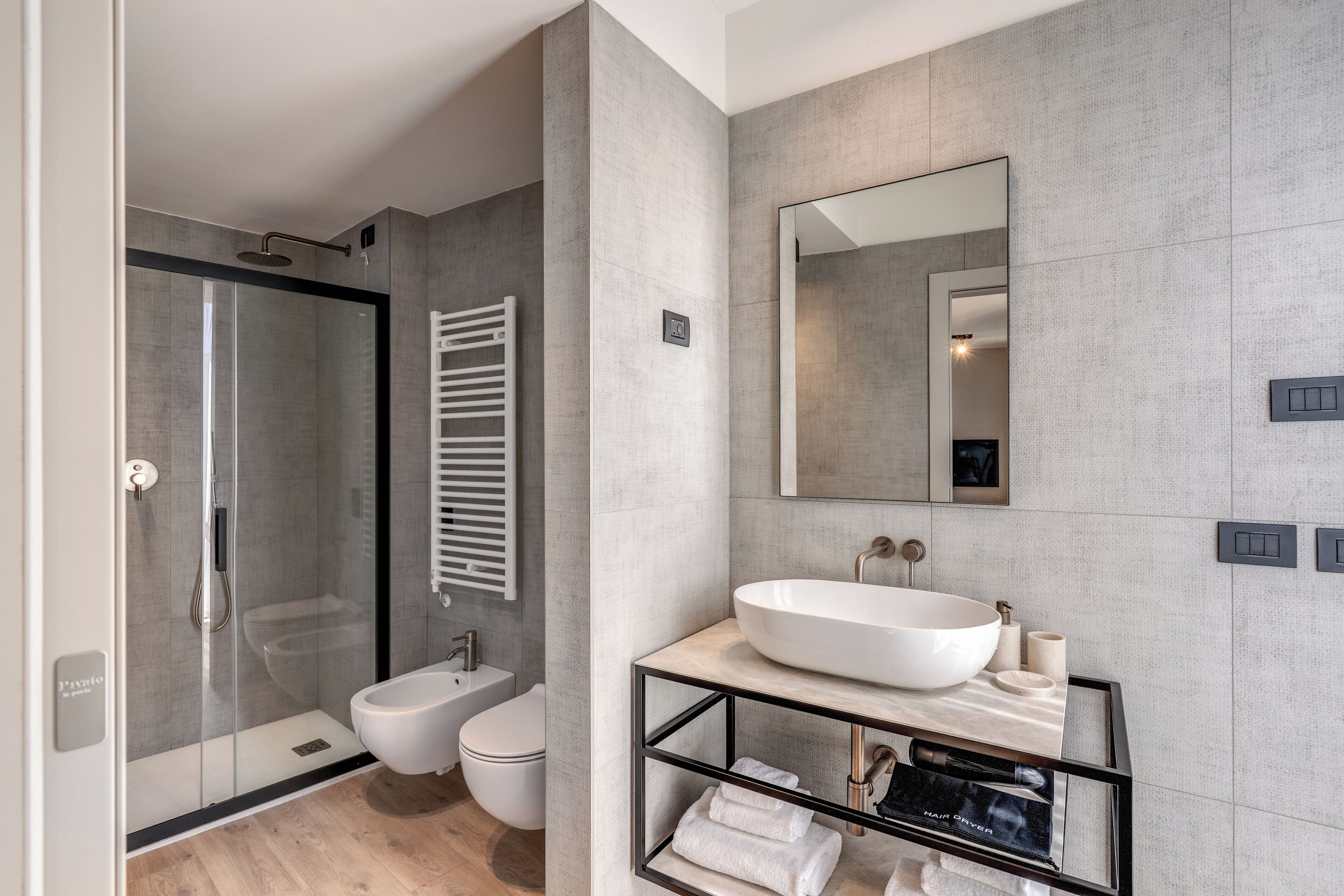 A modern bathroom with a glass-enclosed shower, a toilet, a large sink with a mirror, and a towel rack.