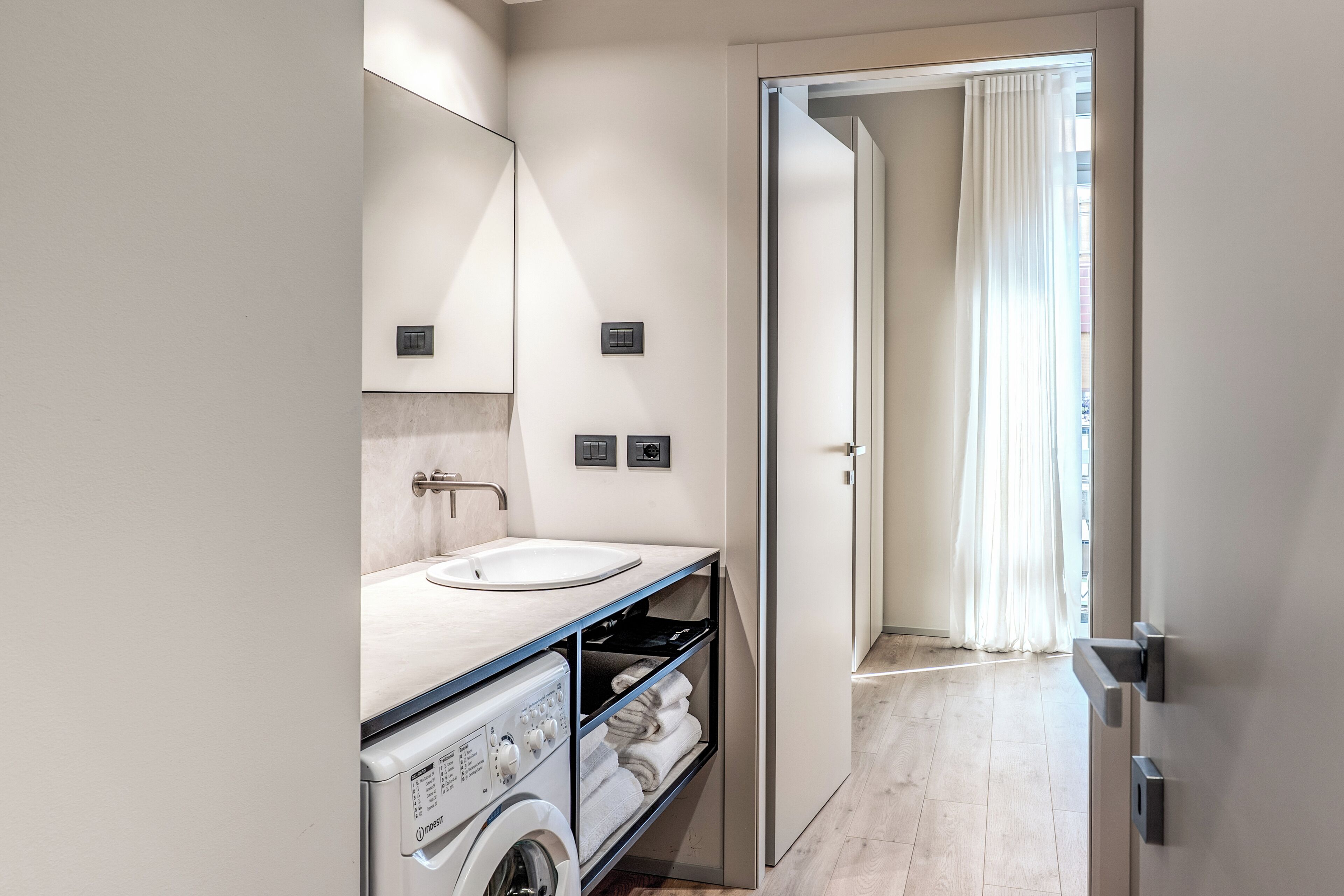 Une salle de bain moderne équipée d’un lave-linge intégré, d’un lavabo et d’un miroir.