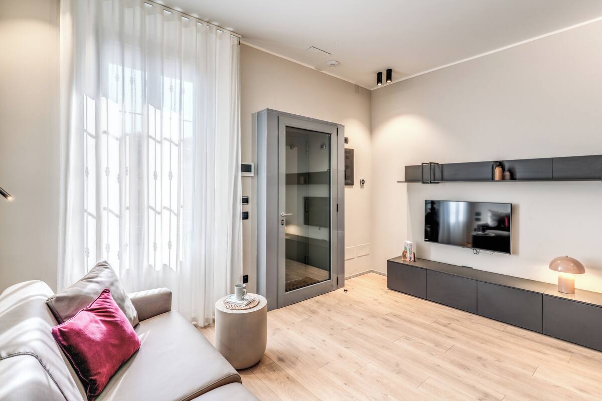 A modern living room with a sofa, a glass door, a flat-screen TV, and a wooden floor.