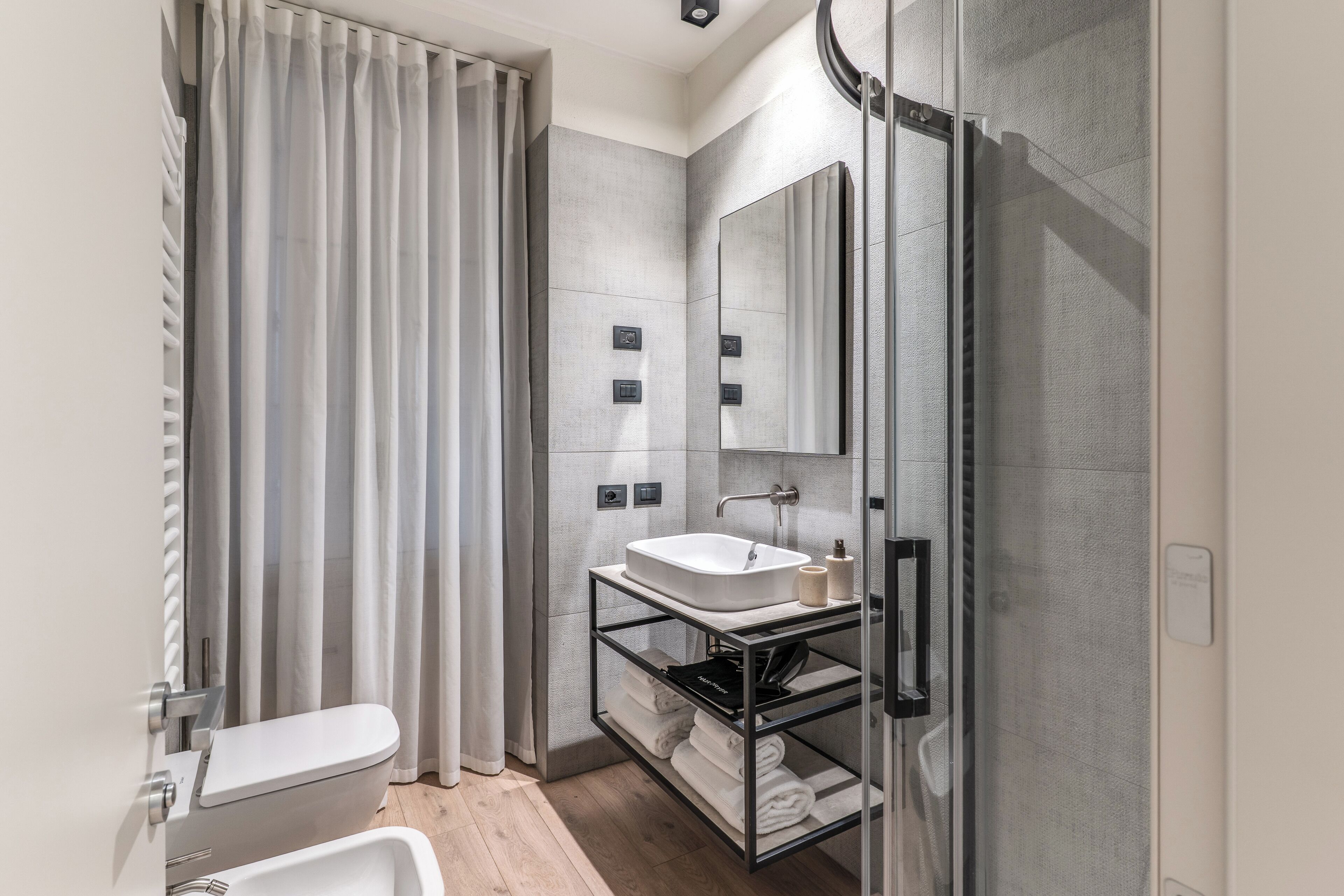A modern bathroom with a glass shower enclosure, a white sink, and a towel rack.