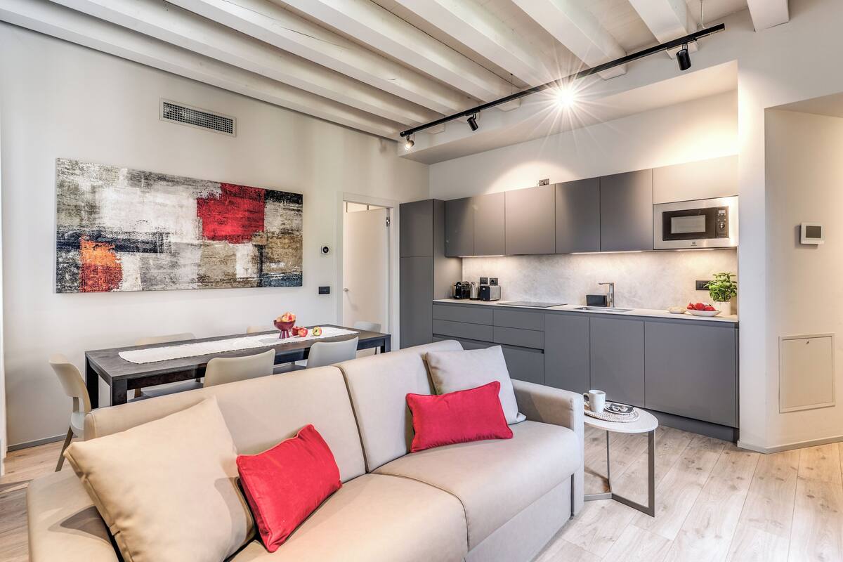 A modern living room with a sofa, a dining table, and a kitchen area with grey cabinets and a microwave.
