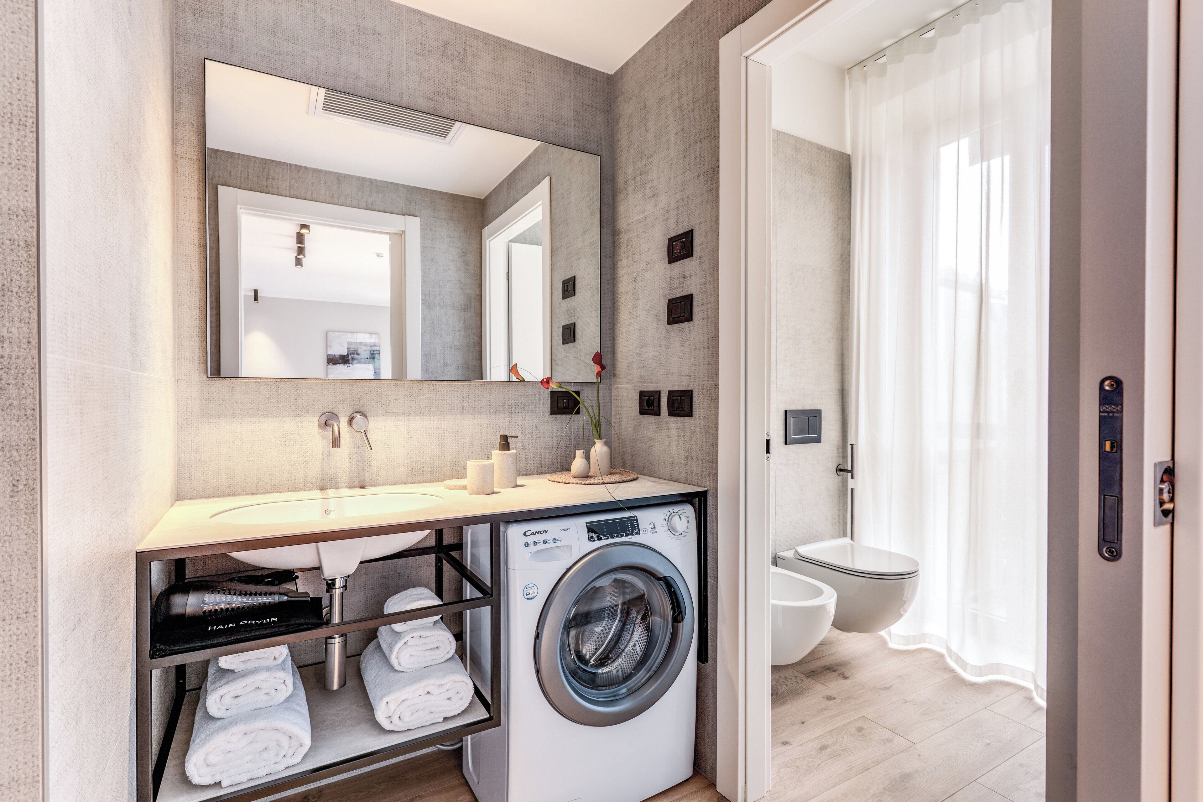 A modern bathroom with a built-in washing machine, a large mirror, and a toilet.