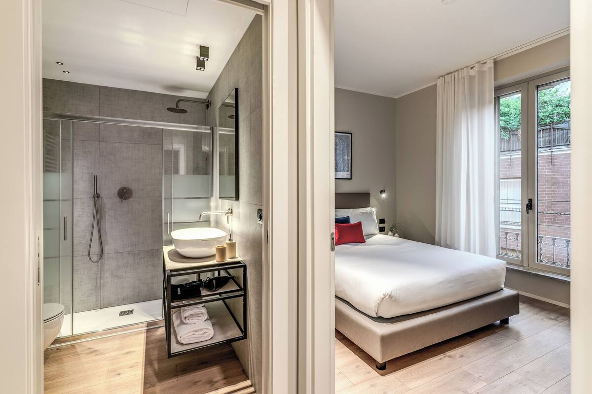 A modern bedroom with a large bed, a bedside table, a mirror, and a window with curtains.