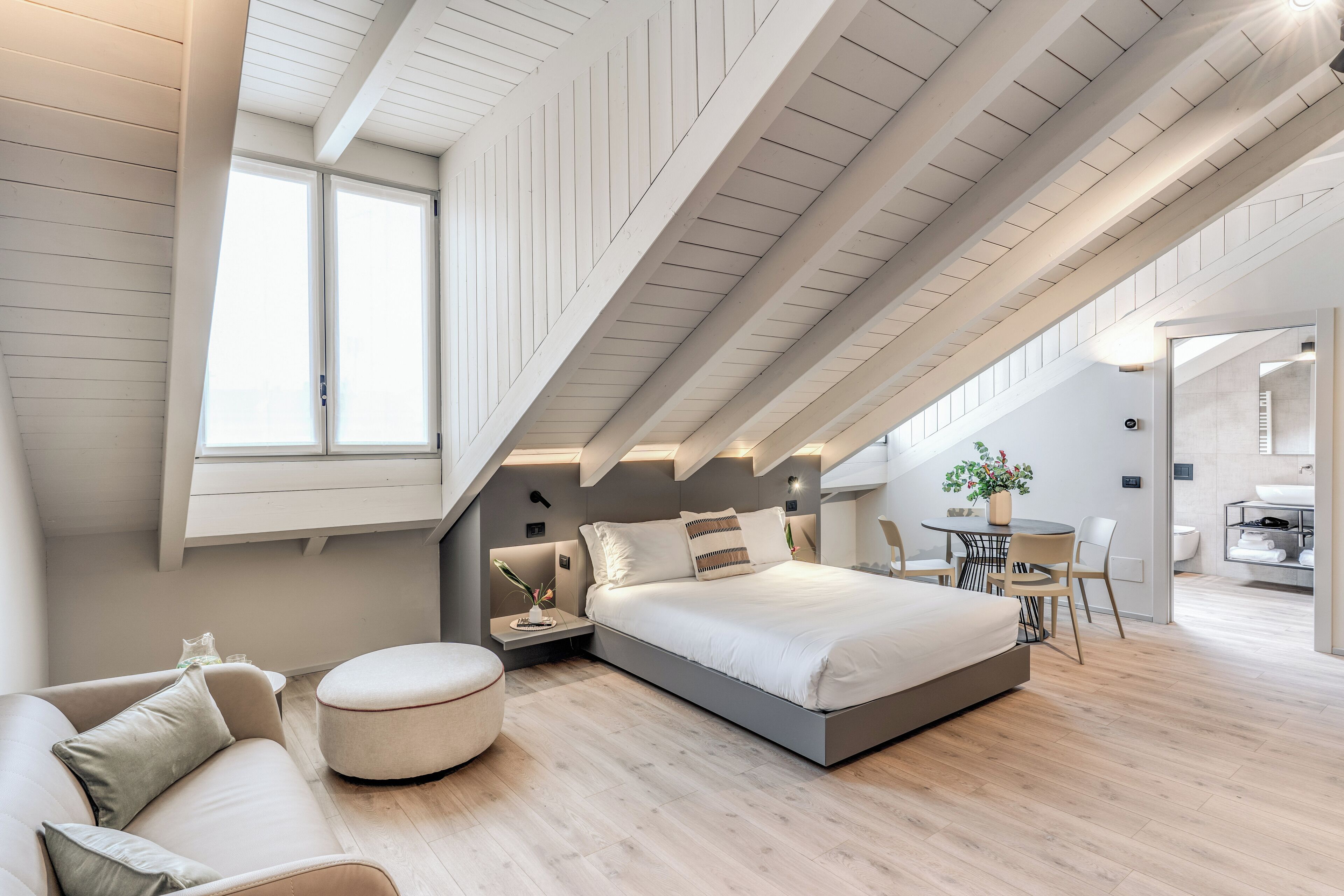 A modern bedroom with a loft-style ceiling, a bed, a seating area, and a dining table.