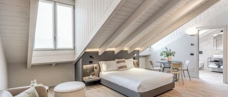 A modern bedroom with a loft-style ceiling, a bed, a seating area, and a dining table.