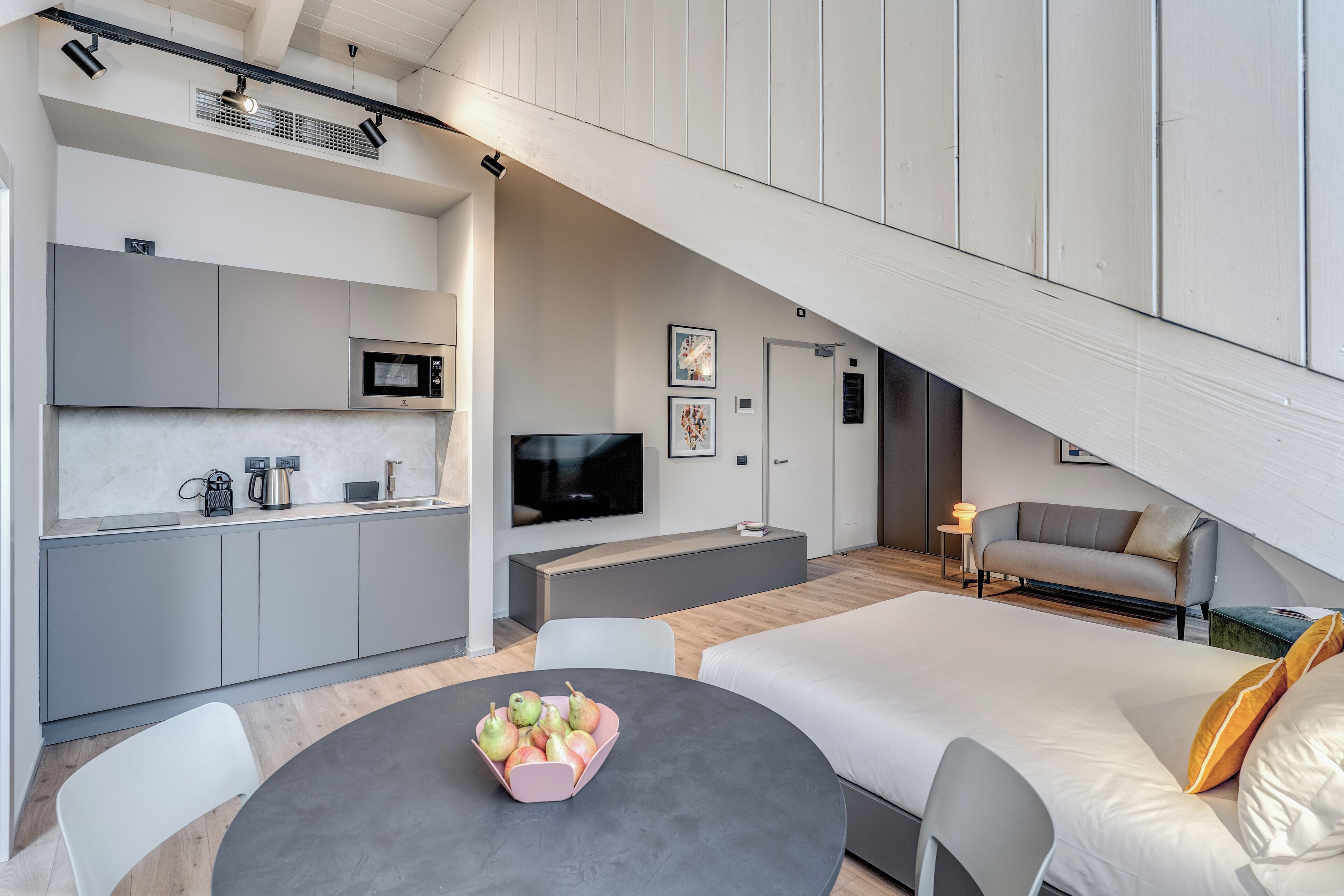 A modern hotel room with a kitchen, a dining area, and a large bed.