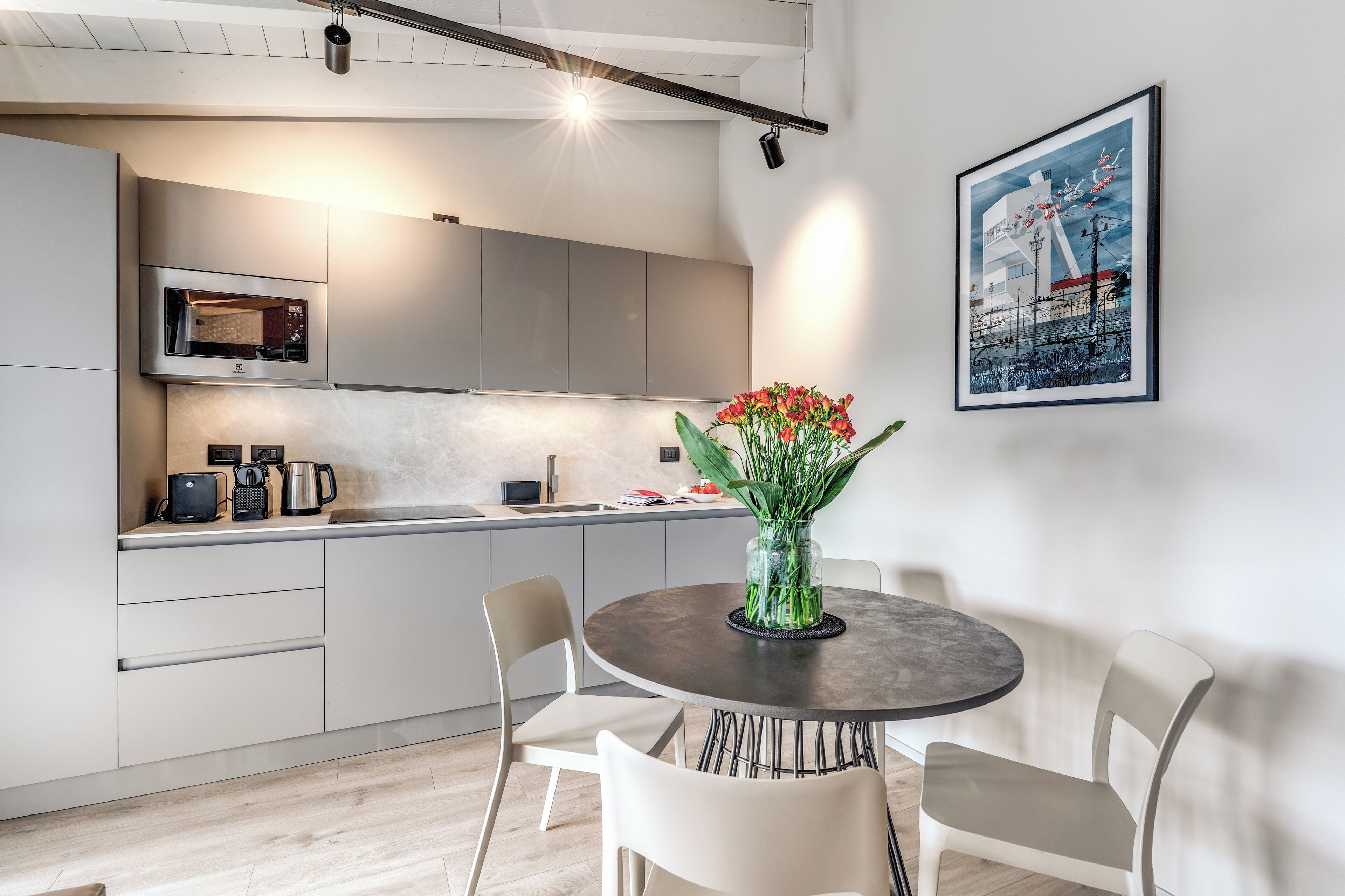 Une cuisine moderne dotée d’appareils électroménagers intégrés, un coin repas avec une table ronde et des chaises, et une œuvre d’art encadrée au mur.